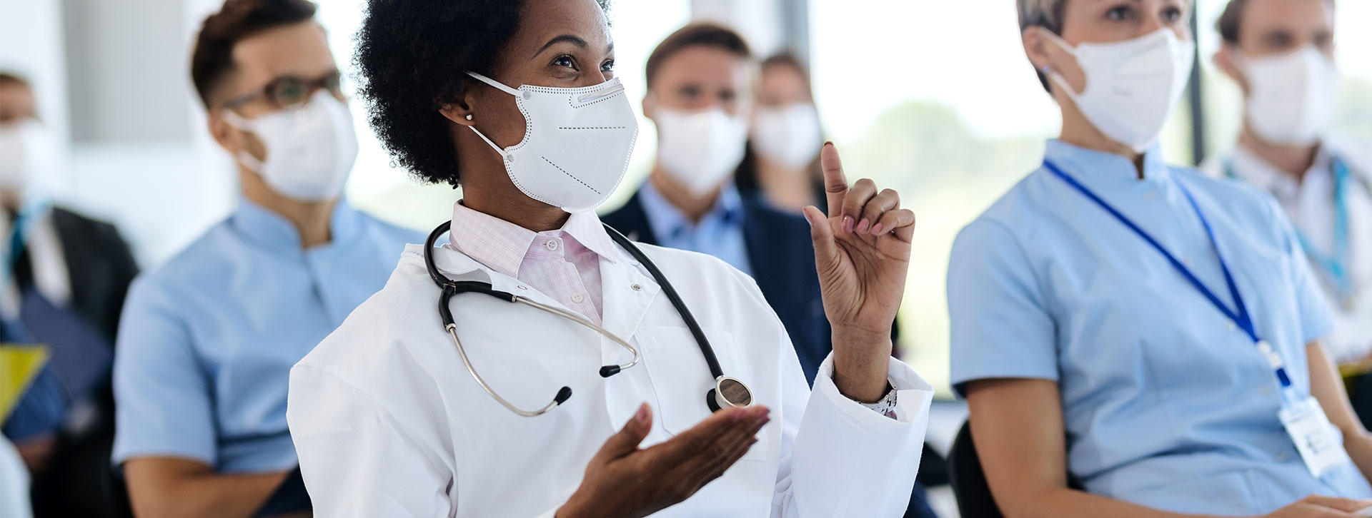 African American female doctor with face mask asking a question while attending a seminar in board room.