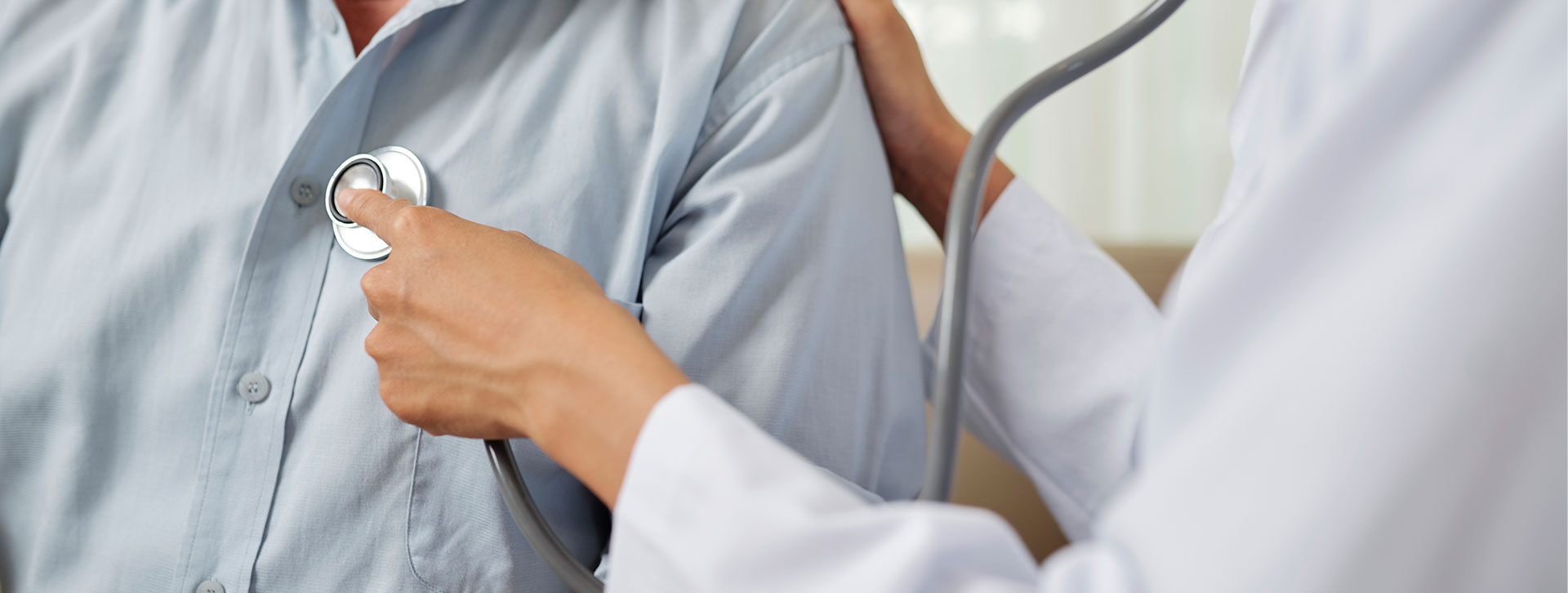 Close-up of female doctor in white coat listening to breathe of senior man during his visit at hospital.