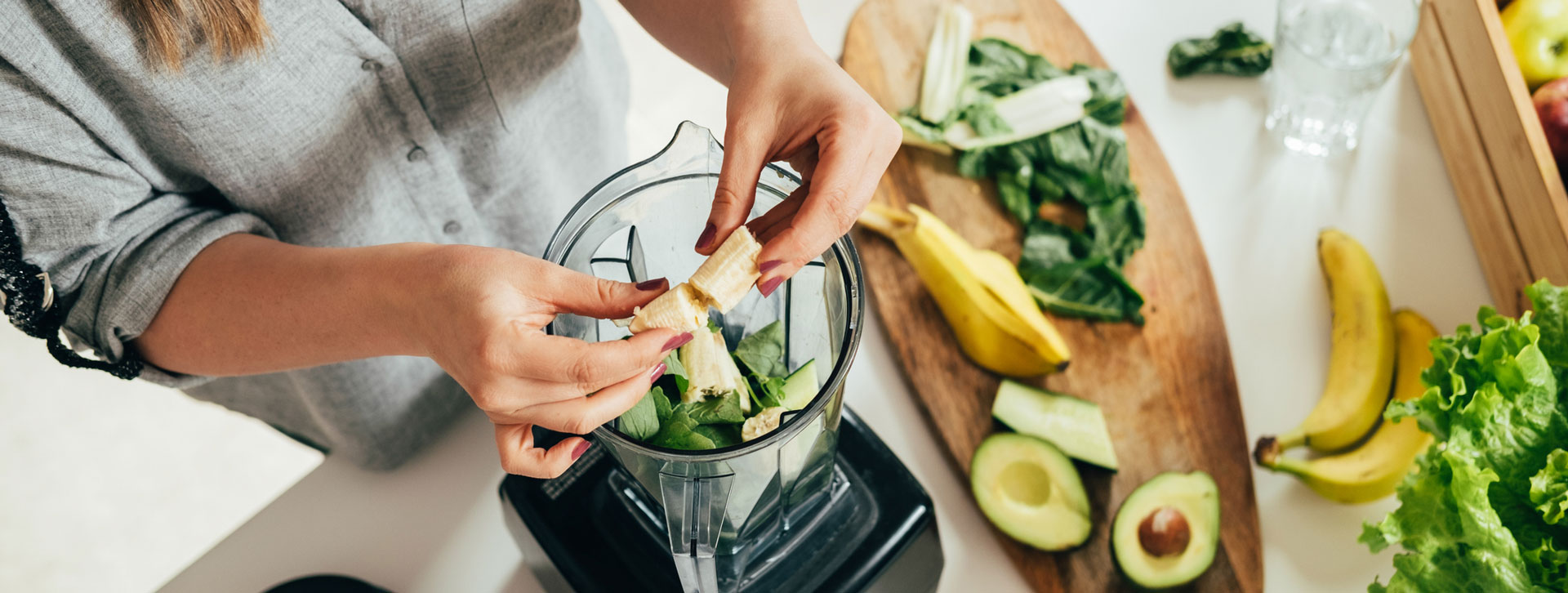 Woman is preparing a green smoothie with fresh fruits, green spinach and avocado.