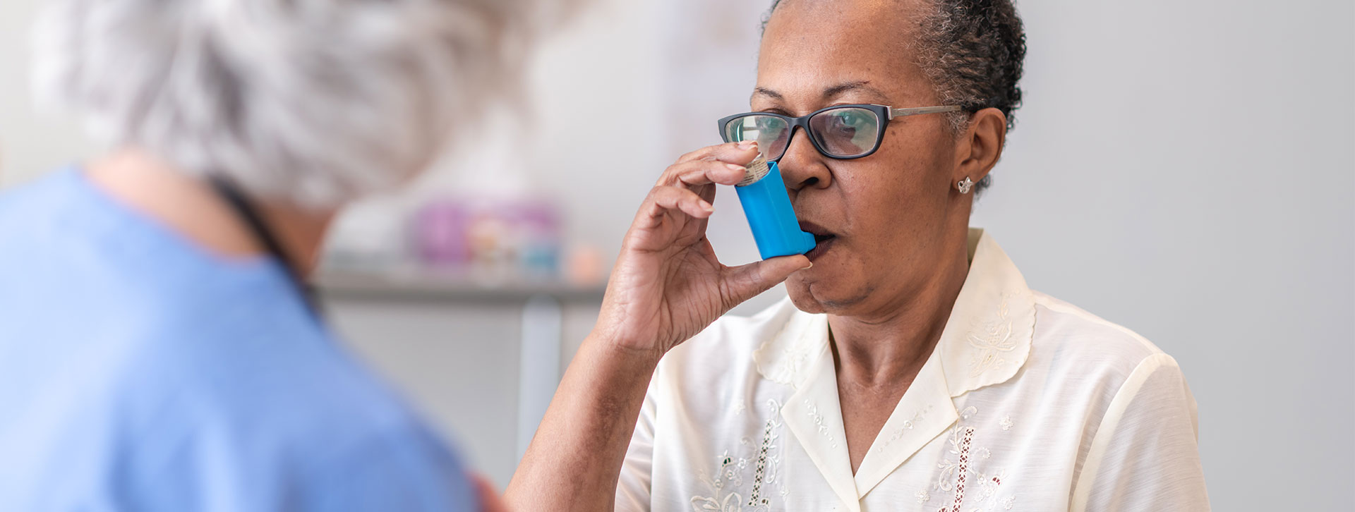 A senior black women is learning how to use an inhaler. 