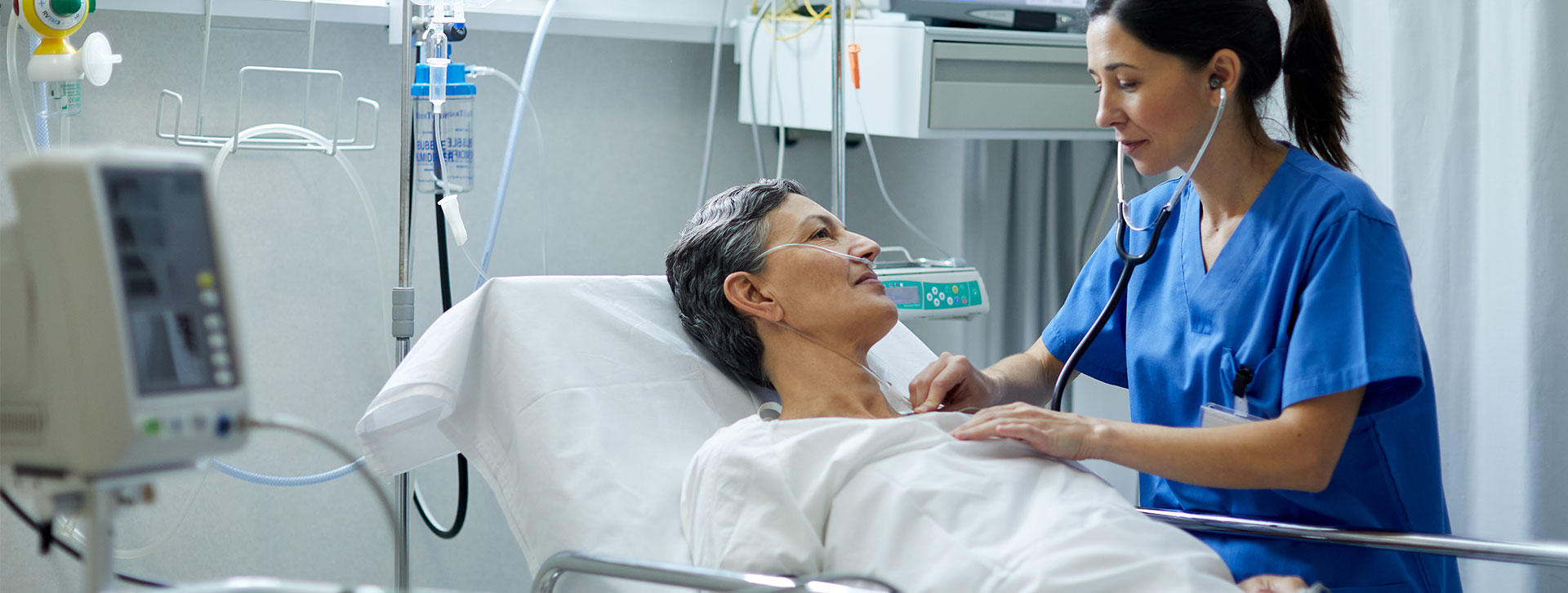 A female nurse is listening with a stethoscope to the heart beat of a patient.