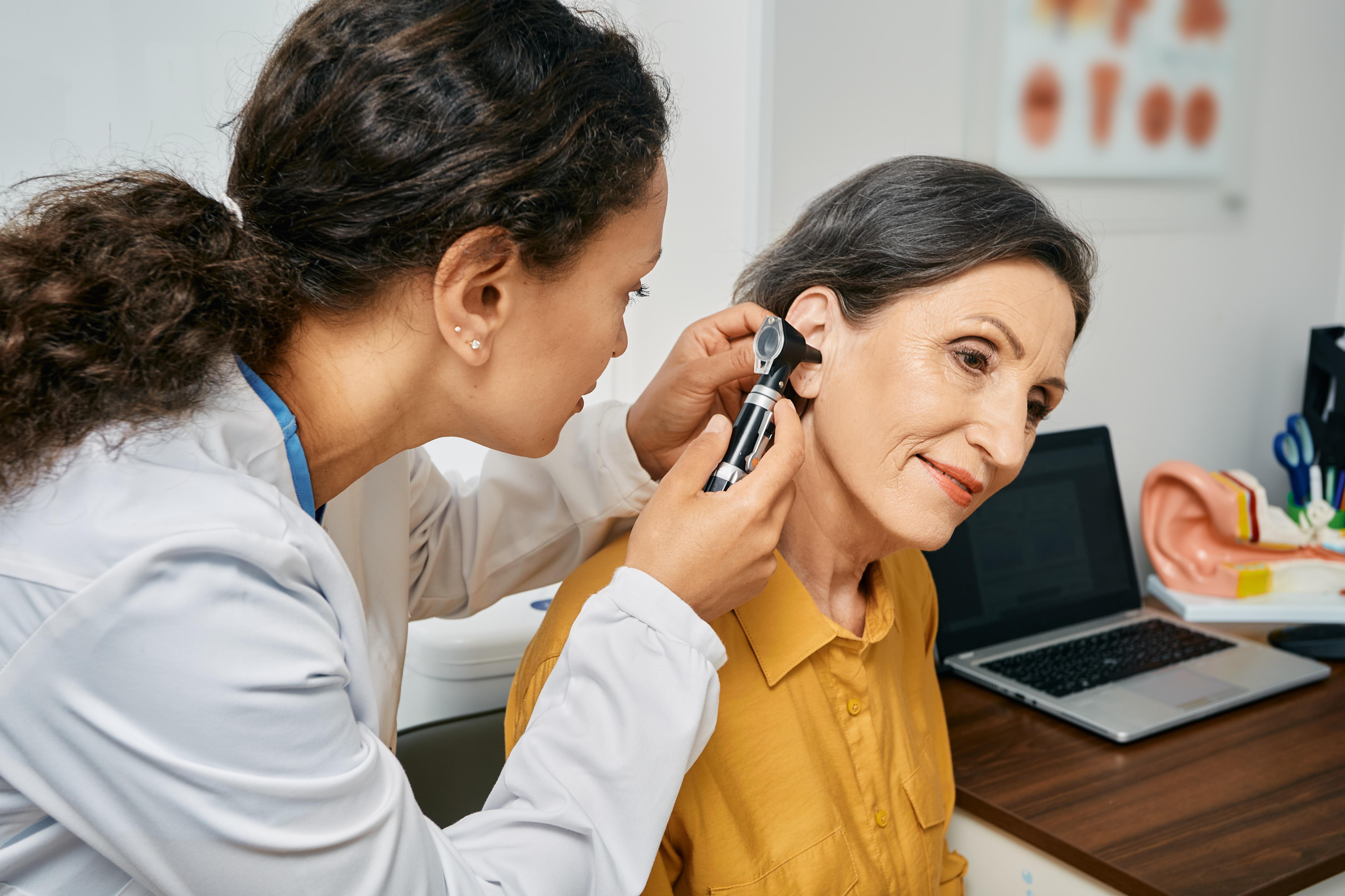 Hearing exam for elderly citizen people. Otolaryngologist doctor checking mature woman's ear using otoscope or auriscope at medical clinic - stock photo