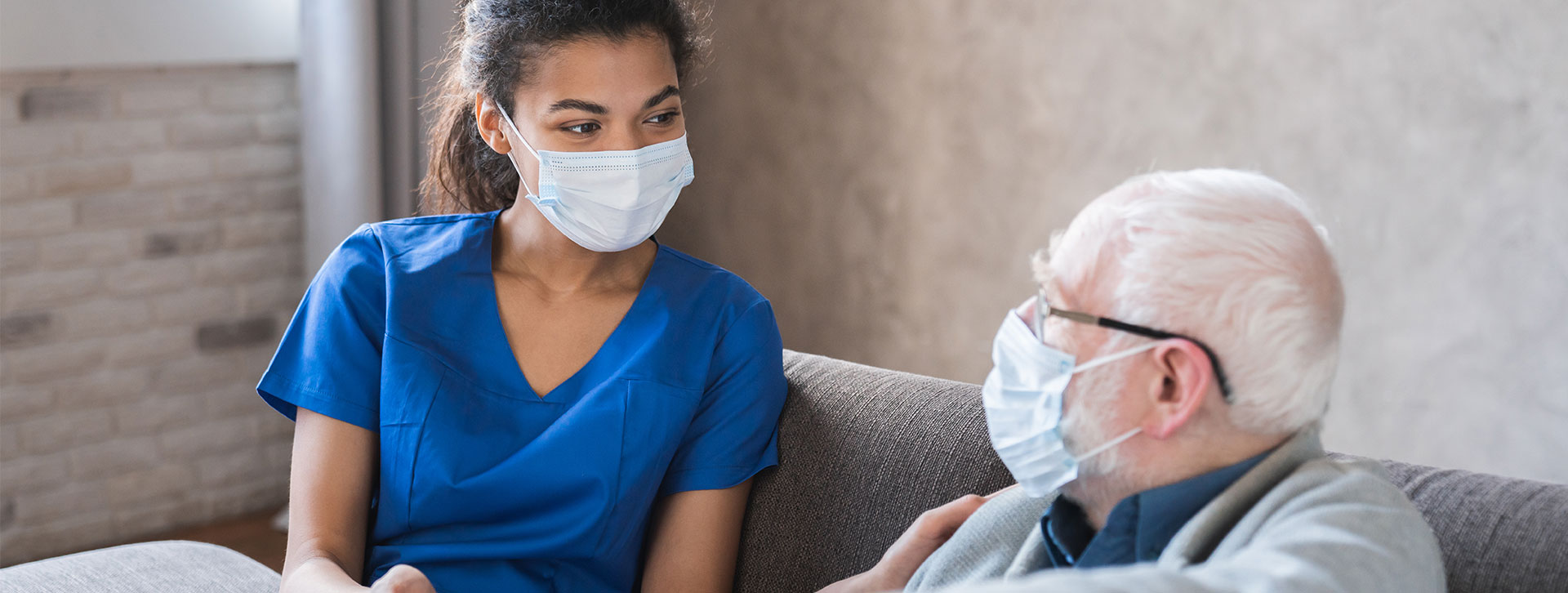 Doctor or female caregiver with senior man wearing protective mask at nursing home.