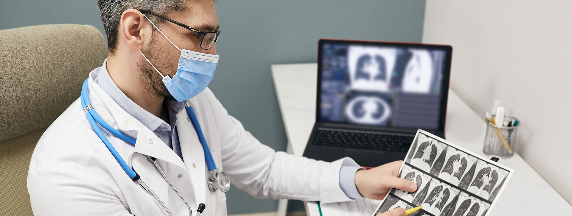 Doctor wearing a protective face mask analyzes results of a patient's lungs CT scan at a medical clinic.