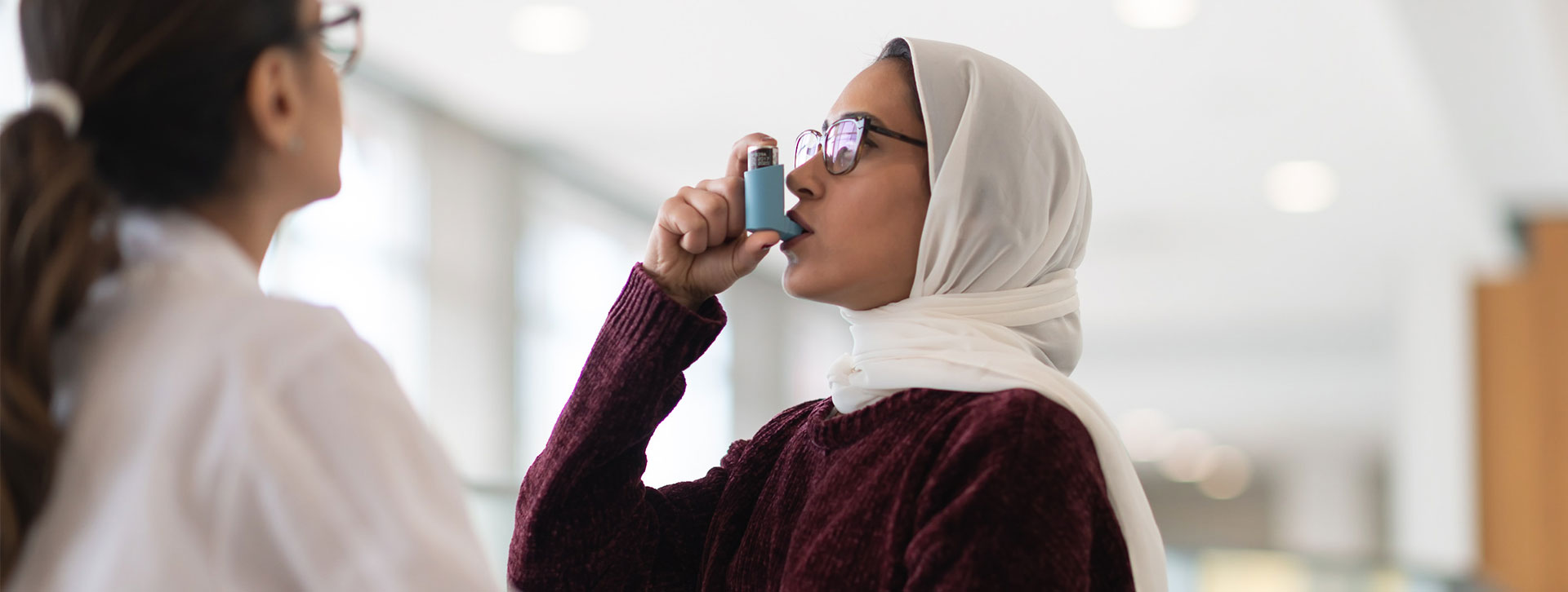 A Muslim woman tests her puffer for her asthma treatment with doctor watching. 