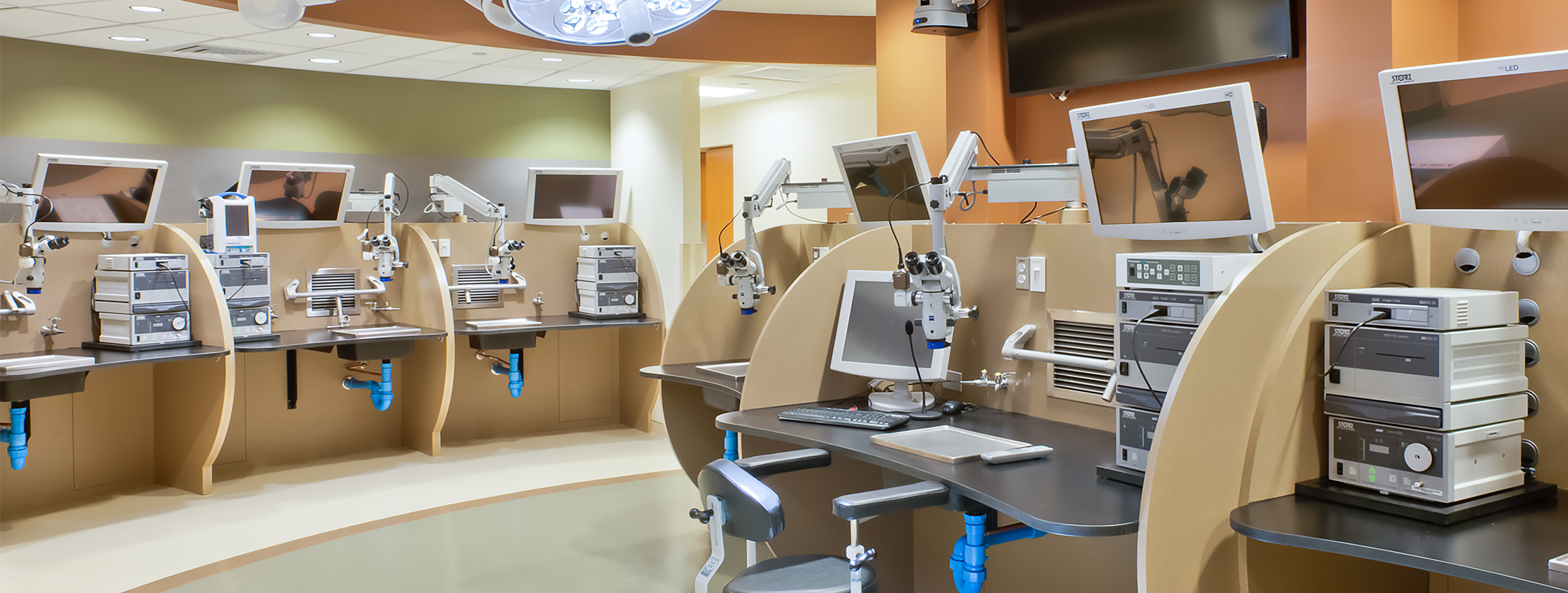 Room with multiple lab stations featuring microscopes and screens.