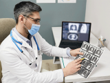 Doctor wearing a protective face mask analyzes results of a patient's lungs CT scan at a medical clinic.