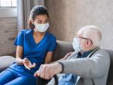 Doctor or female caregiver with senior man grandfather wearing protective mask to protect from Covid 19 at home or nursing home. Doctor talking consulting elderly patient at home