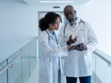 Two doctors standing in white coats looking at a tablet.