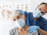 Male doctor examining an older female patient's neck.