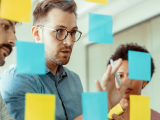 four people working on a glass board with sticky notes.