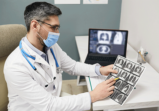 Doctor wearing a protective face mask analyzes results of a patient's lungs CT scan at a medical clinic.