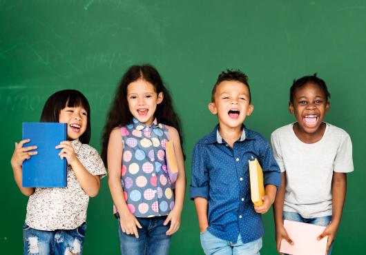 Four children standing together smiling and holding books.