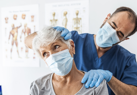 Male doctor examining an older female patient's neck.