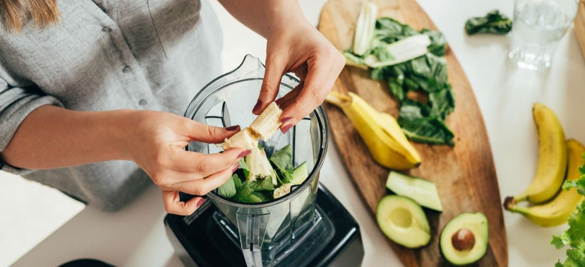 Woman is preparing a green smoothie with fresh fruits, green spinach and avocado.